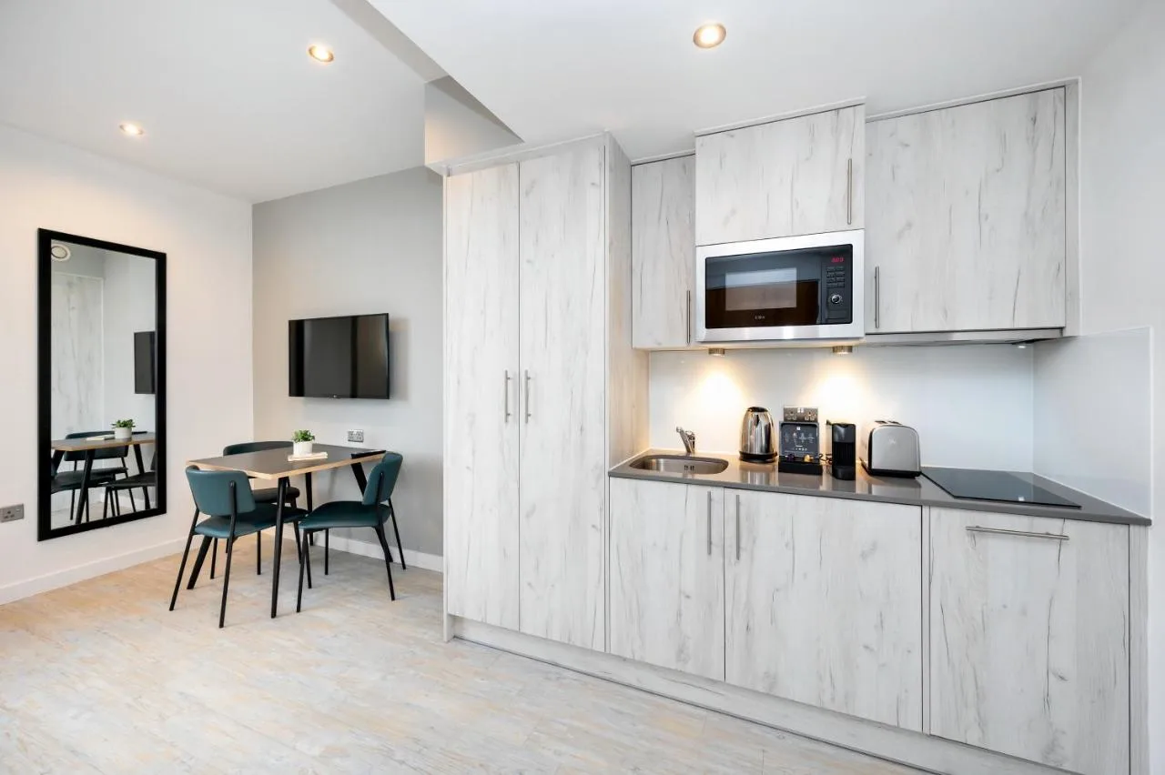 a kitchen with white cabinets and a table with chairs at Staycity Aparthotels Liverpool Waterfront in Liverpool